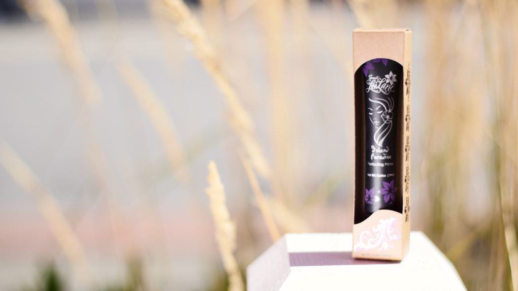 A photo of the Sweet LeiLani skin primer in its packaging sitting in front of wheat grass.